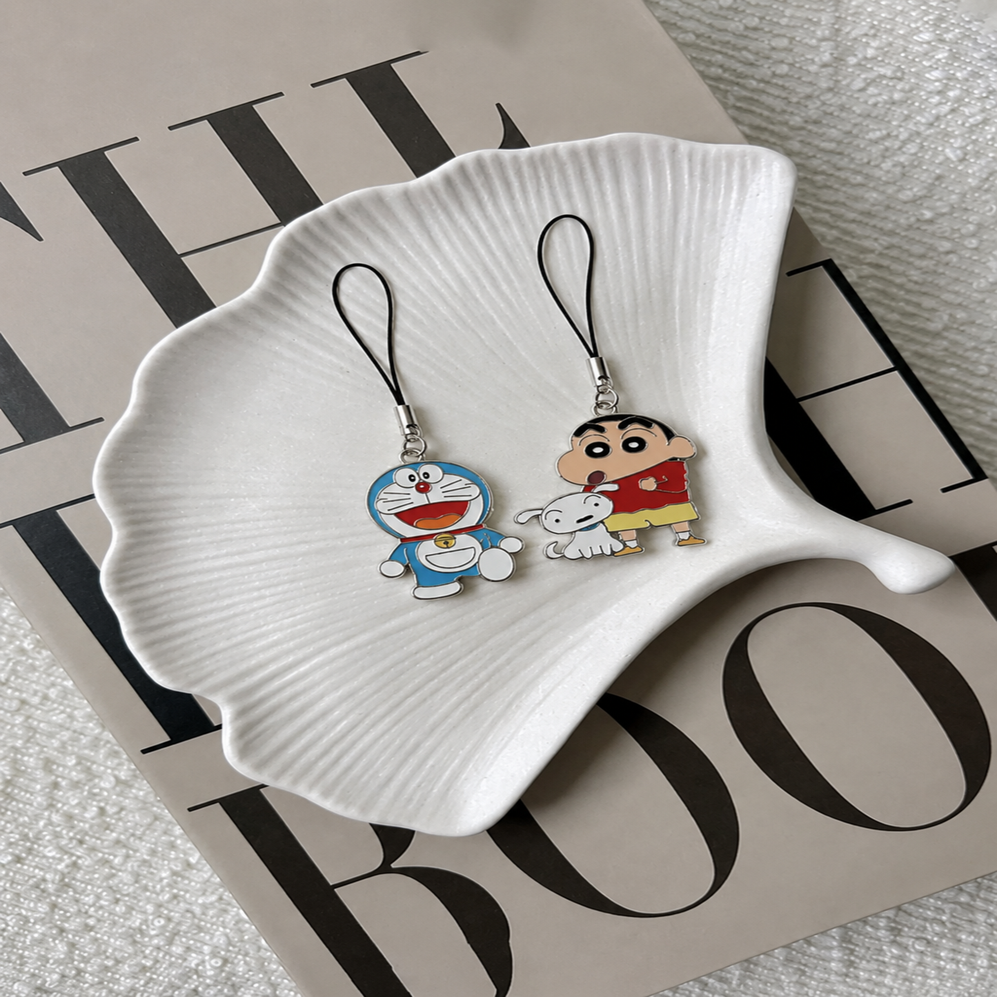 Two cartoon-themed phone charms on a white dish with a magazine background