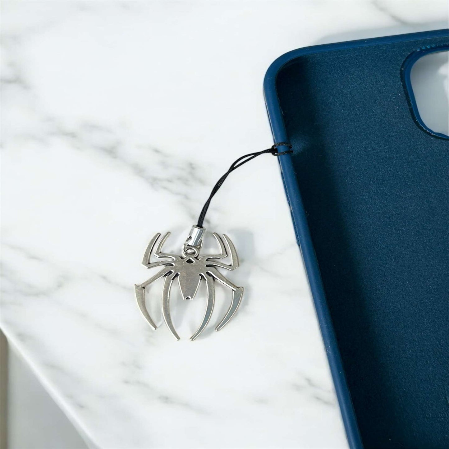 Spider-shaped phone charm attached to a blue phone case on a white marble surface - Thecharmingcharms09