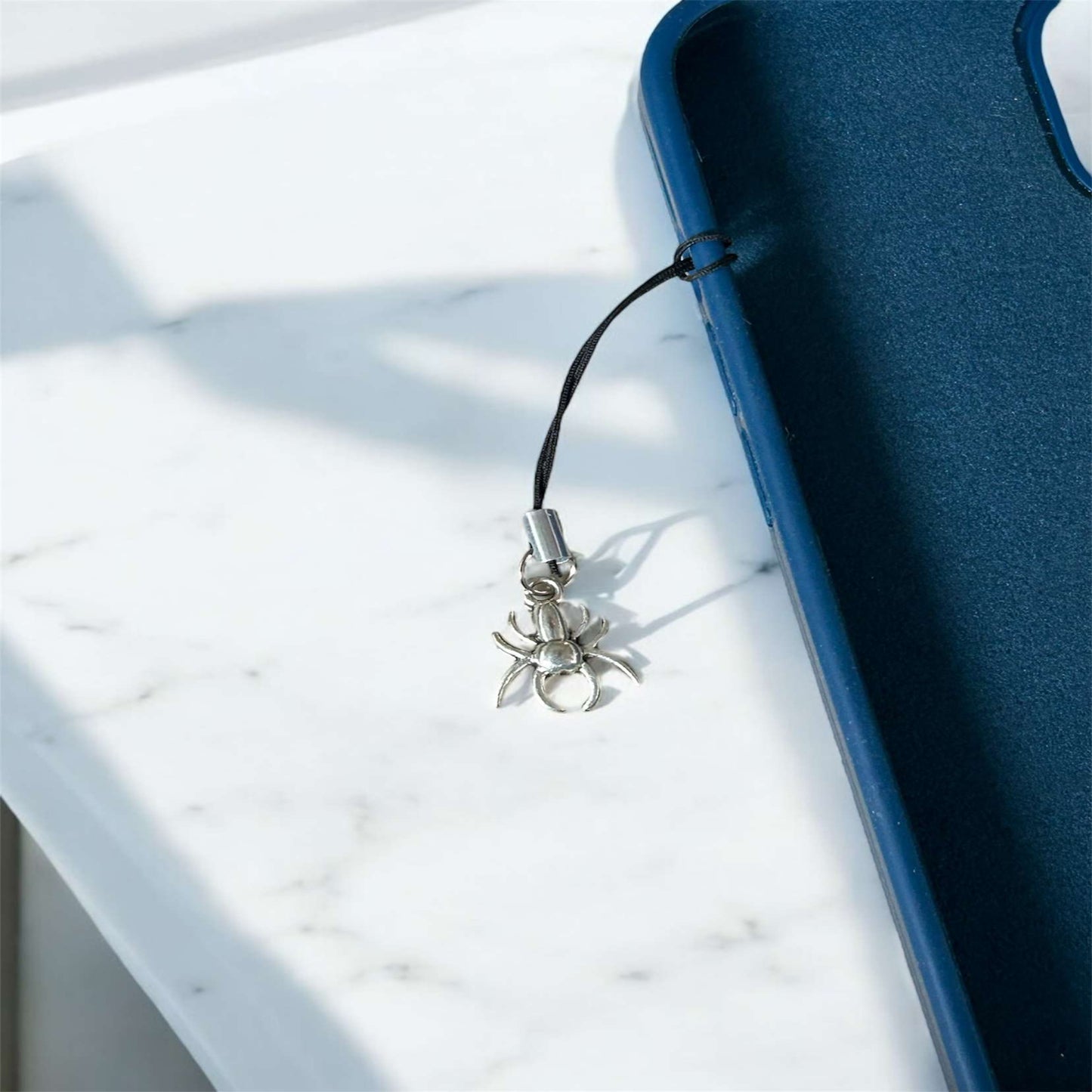 Spider-shaped phone charm attached to a blue phone case on a marble surface - Thecharmingcharms09