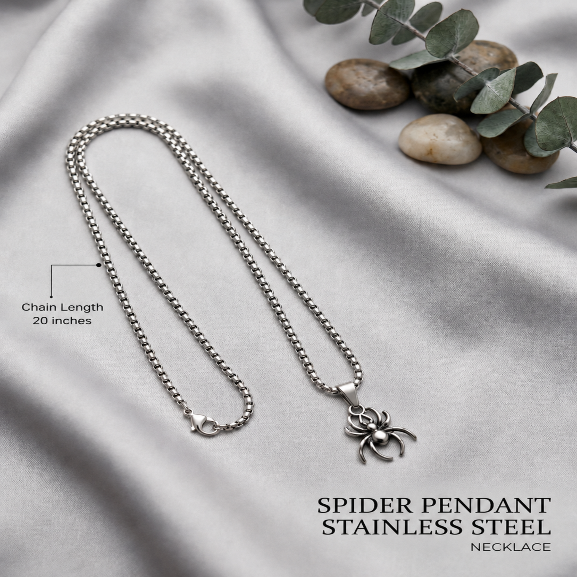 Spider pendant stainless steel necklace on a gray fabric background with eucalyptus leaves.