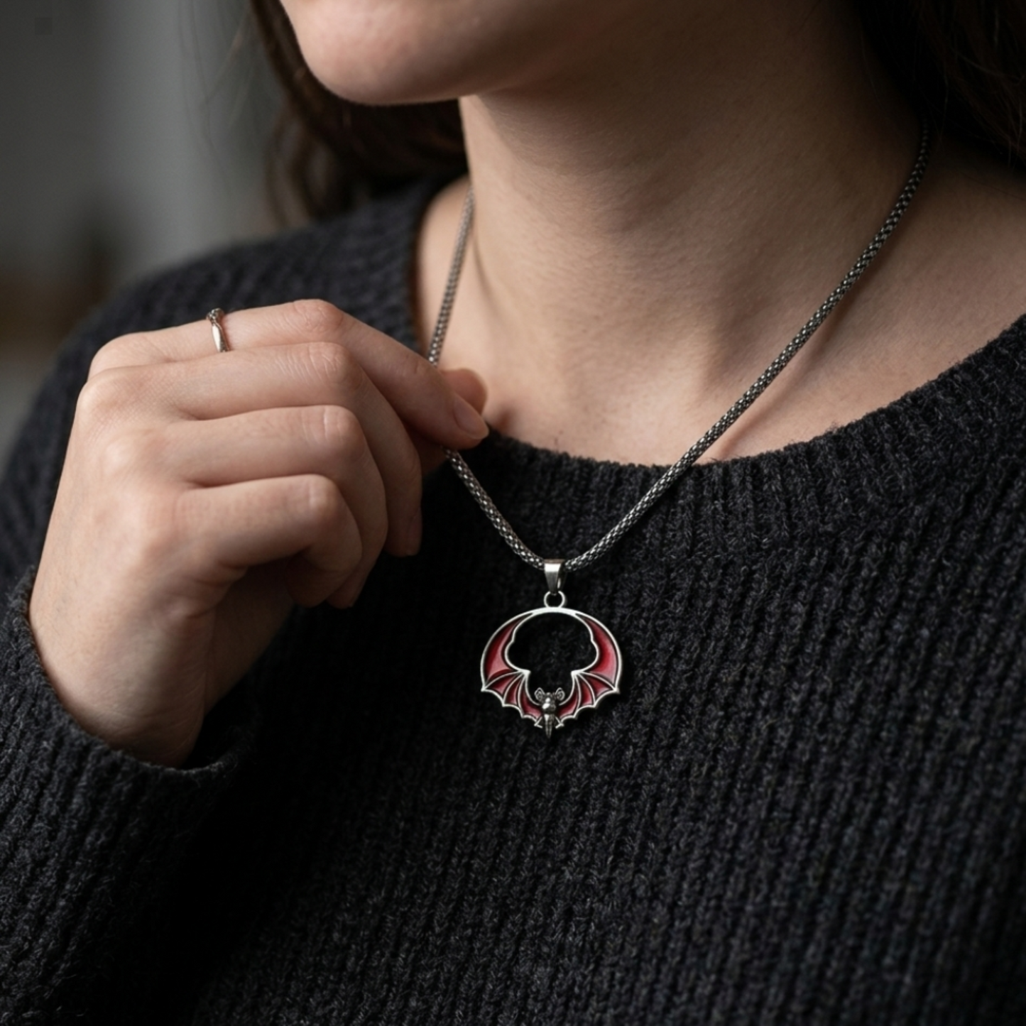 Person wearing a black sweater with a necklace featuring a circular pendant.