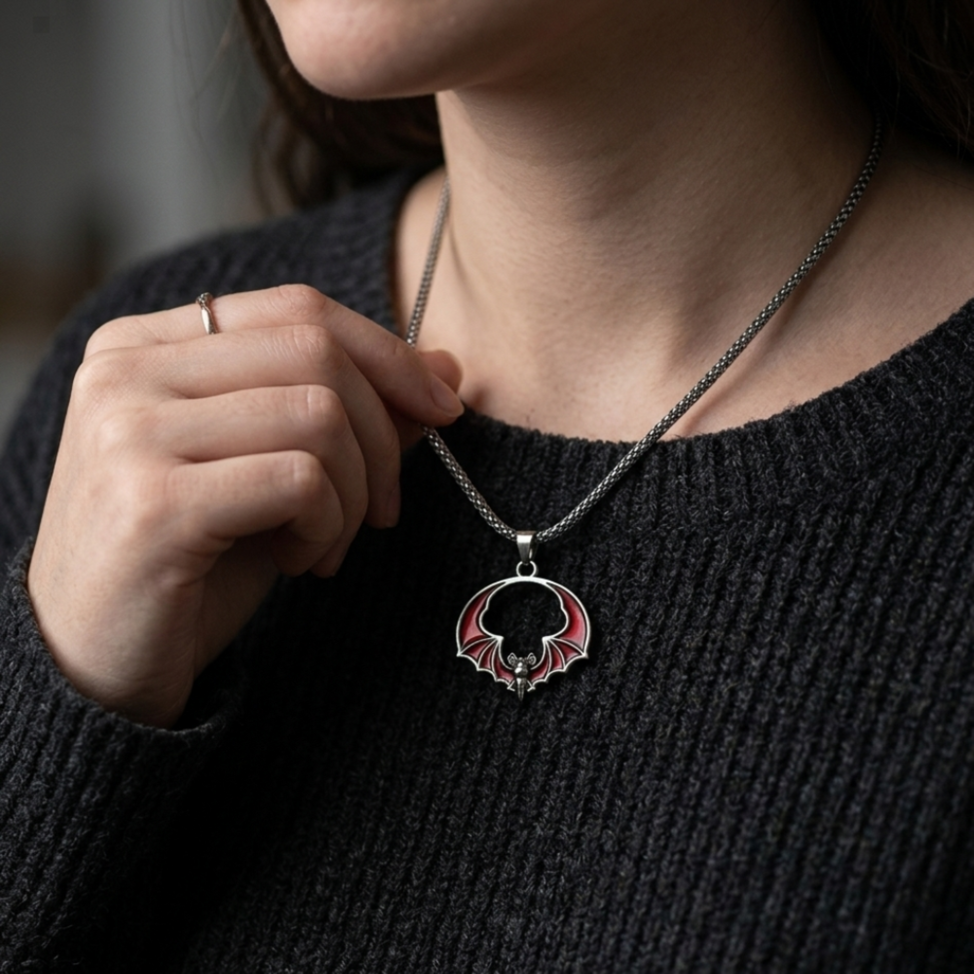 Person wearing a black sweater with a necklace featuring a circular pendant.