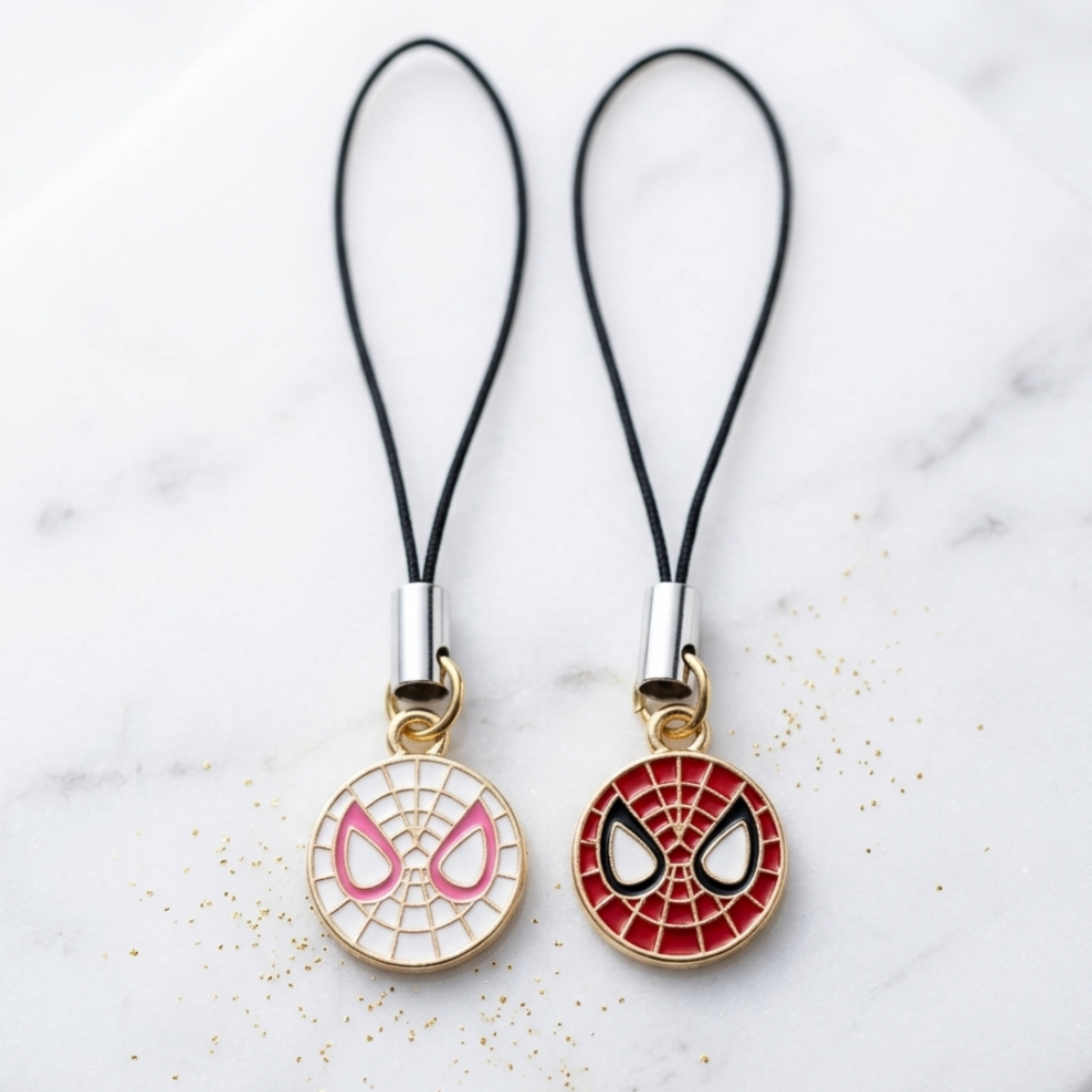 Two spider-themed phone charms on black strings against a marble background