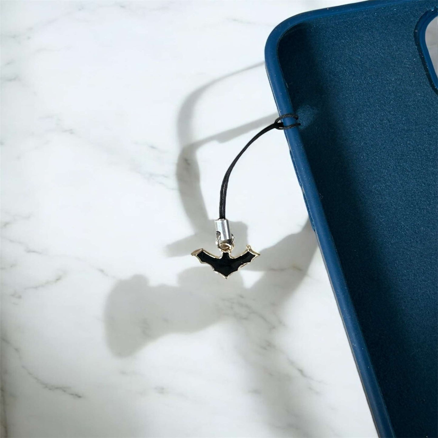 Phone case with a bat-shaped charm on a marble surface - Thecharmingcharms09