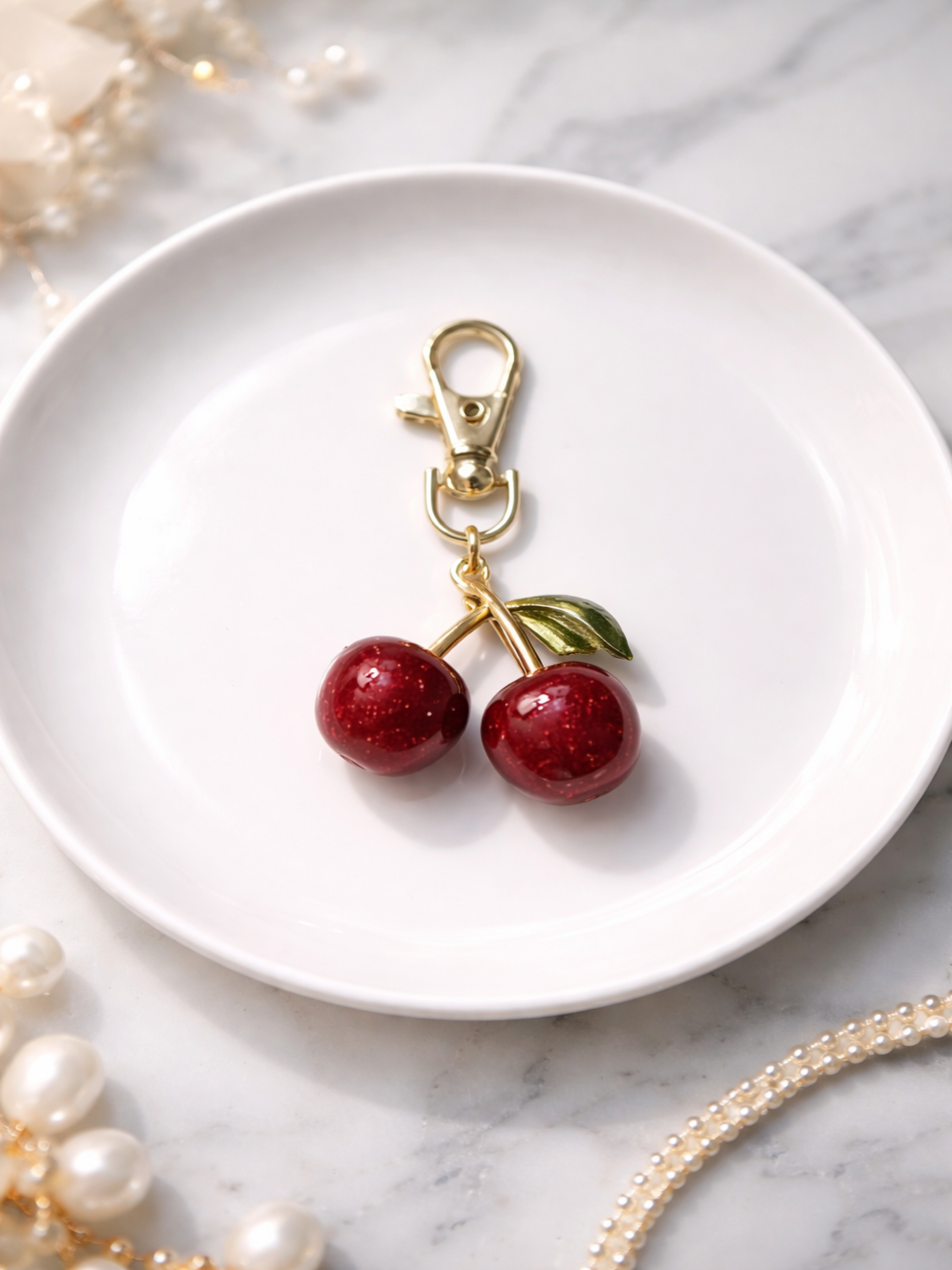 Cherry-shaped keychain on a white plate with pearls in the background