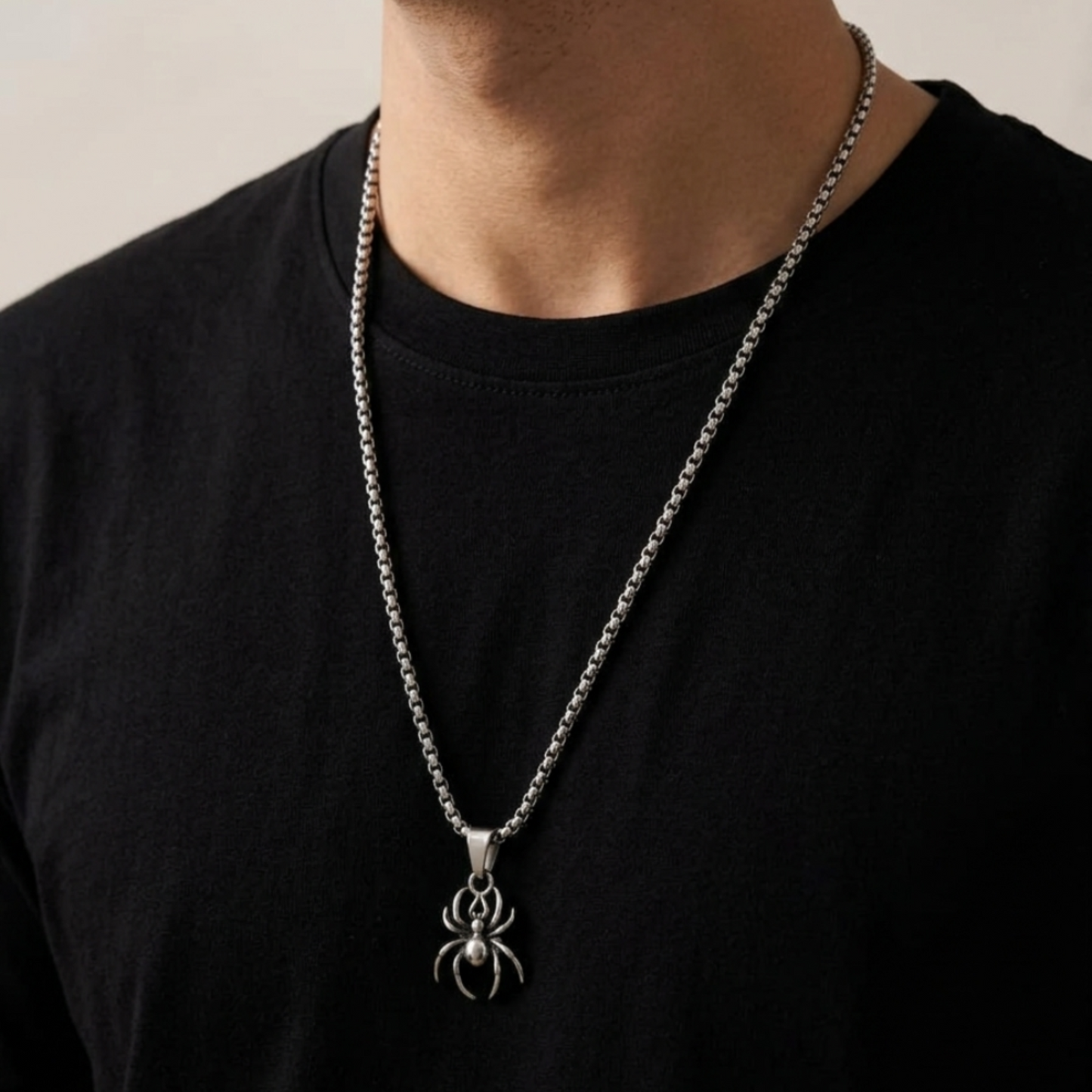 Person wearing a black shirt with a silver chain necklace featuring a spider pendant.